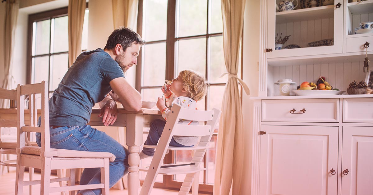 Vater mit Sohn der im Hochstuhl sitzt am Esstisch
